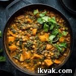 Plant based chickpea, sweet potato and spinach curry in a black cast iron pan on a black background.