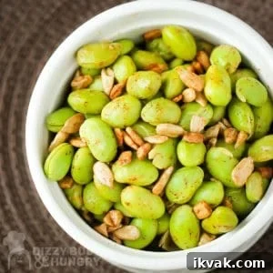 Close up overhead shot of chipotle edamame in a white bowl on a brown surface.