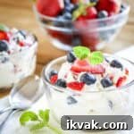 Side shot of a small glass bowl filled with cheesecake fluff topped with fresh blueberries and strawberries.