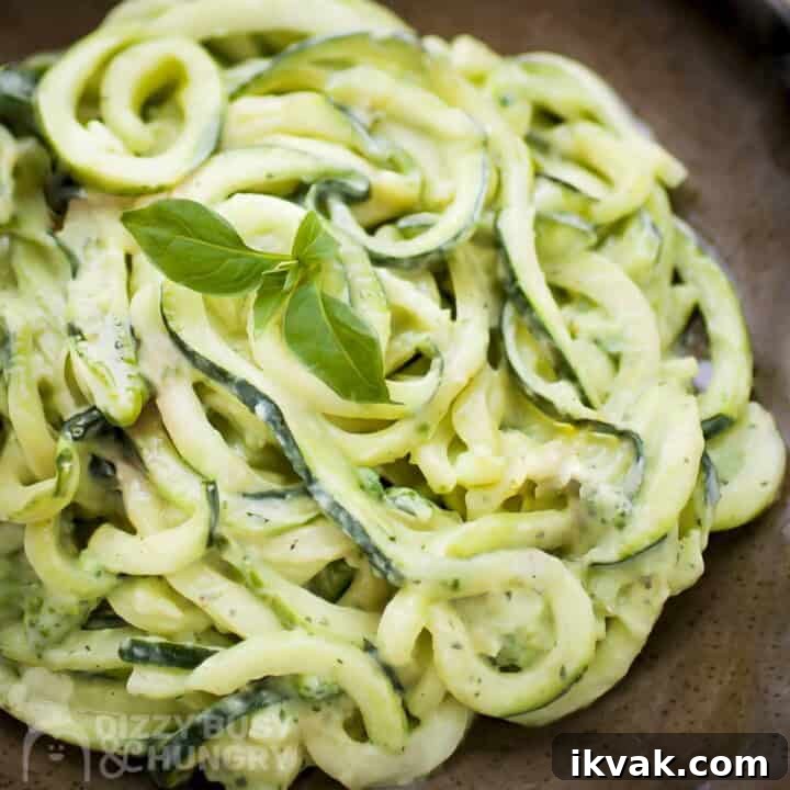 Close up shot of zucchini noodles in avocado sauce garnished with basil in a brown speckled bowl.