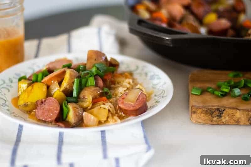 Delicious plate of sausage and potatoes over dirty rice with spicy gravy drizzled overtop.
