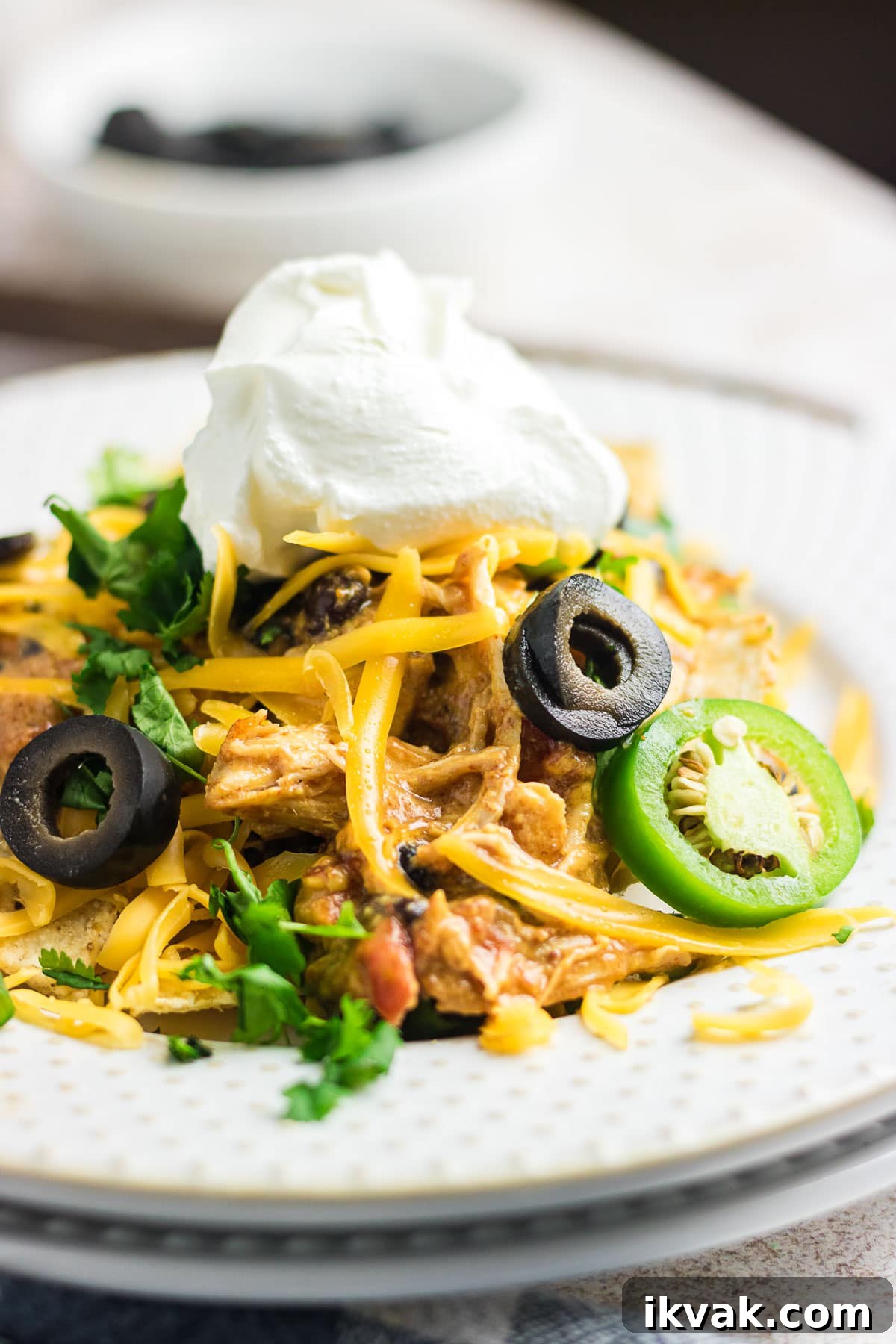 An up-close photo of creamy chicken nachos on a white plate topped with sour cream.