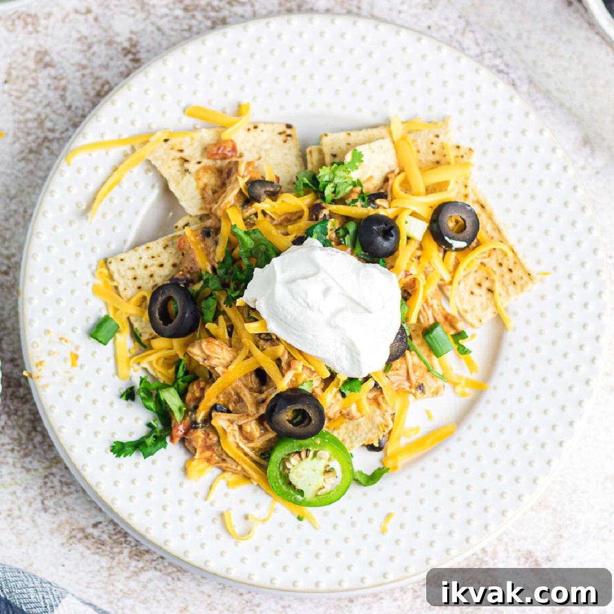 Overhead view of creamy chicken nachos on a plate garnished with sour cream.