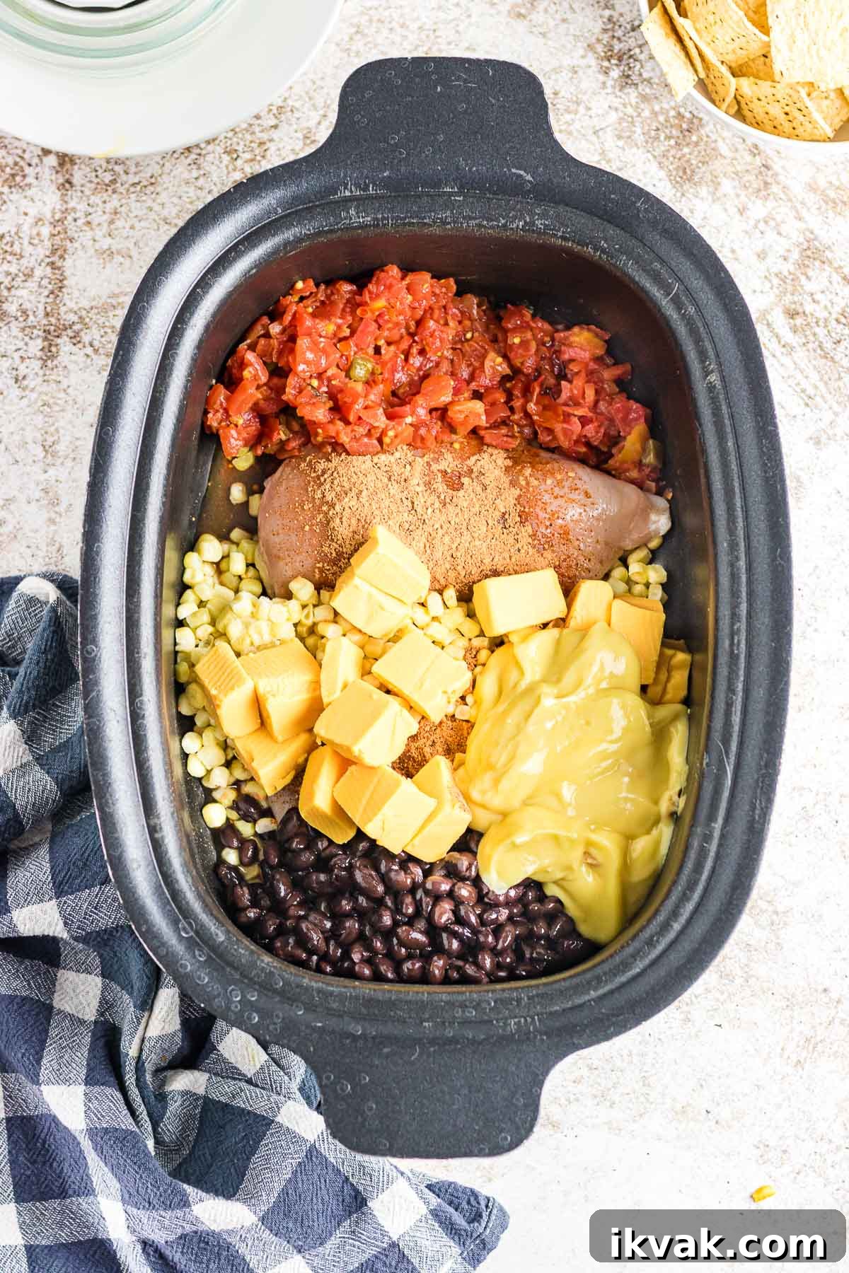 A crockpot filled with chicken, tomatoes, corn, cheese, and beans.