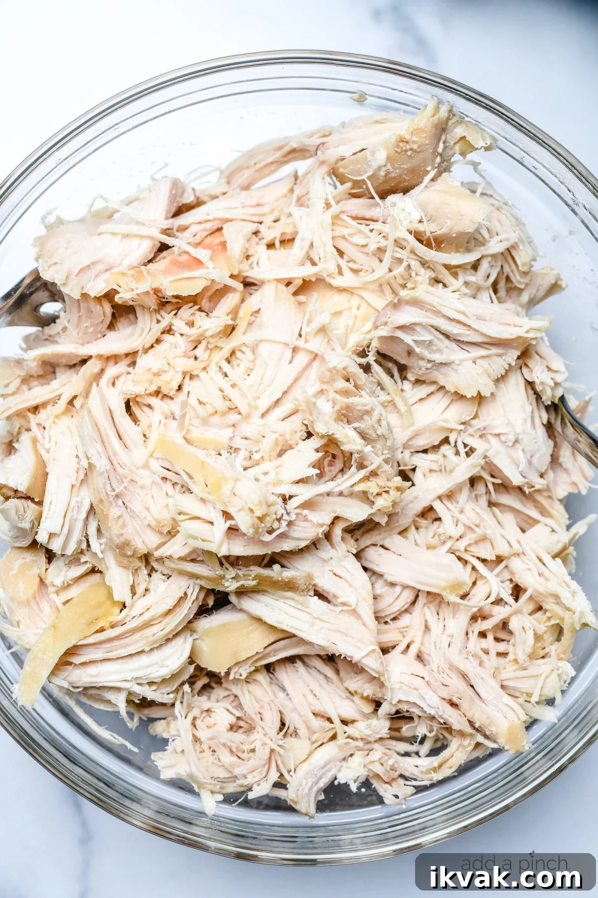 Shredded chicken in a glass bowl ready to be used in recipes.