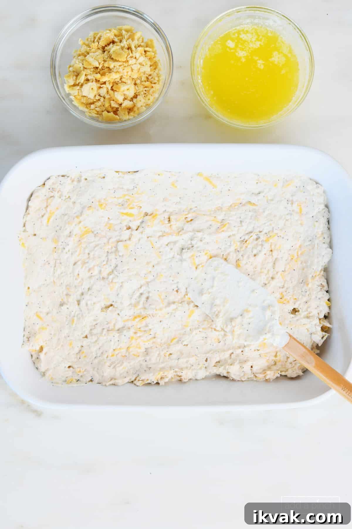 White ceramic baking dish holds the chicken casserole ingredients while a bowl of crushed crackers and melted butter sit to the side waiting to top the dish.