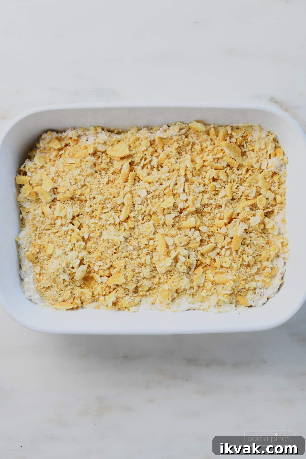 Chicken casserole is topped with buttery cracker topping all in a white baking dish and ready to bake.