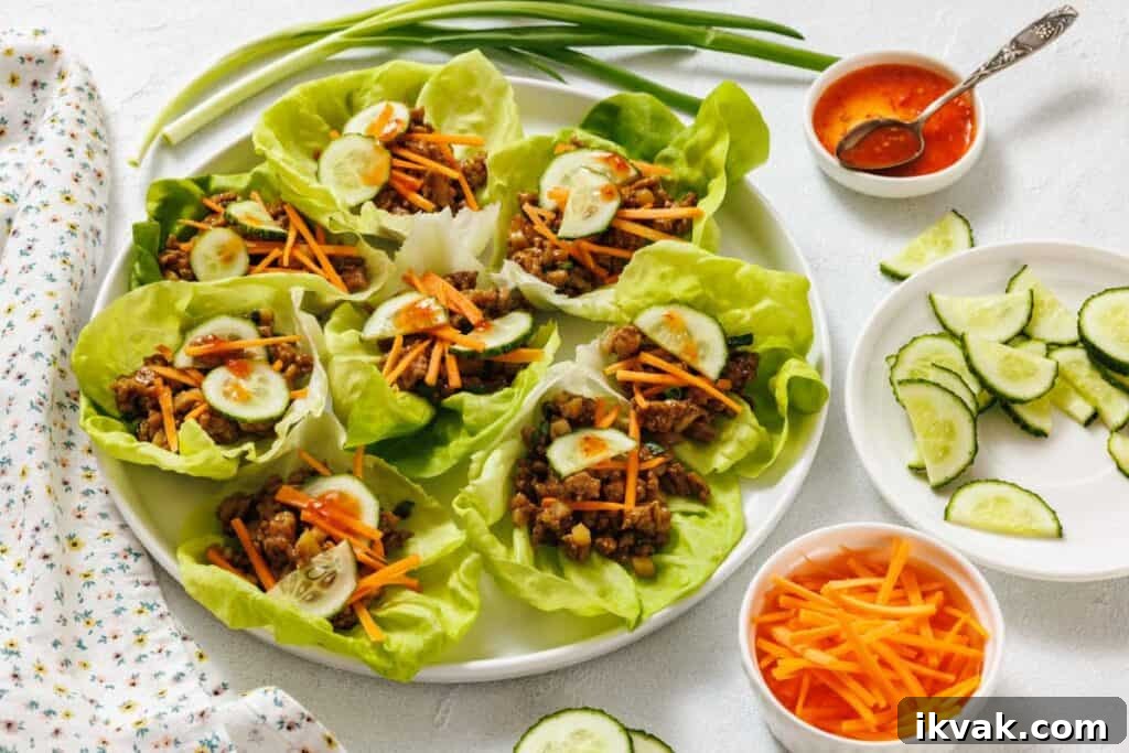 A plate of chicken lettuce wraps filled with shredded carrots and cucumber slices, with bowls of sliced cucumbers, shredded carrots, and dipping sauce on the side.