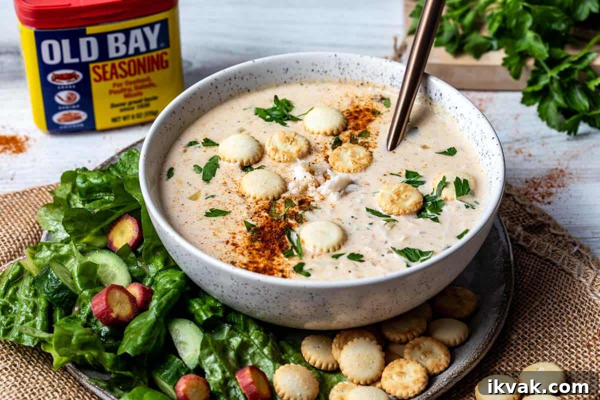 Classic Maryland Cream of Crab Soup Recipe 10 bowl of maryland cream of crab soup on a plate with salad and crackers, in front of container of Old Bay Seasoning.