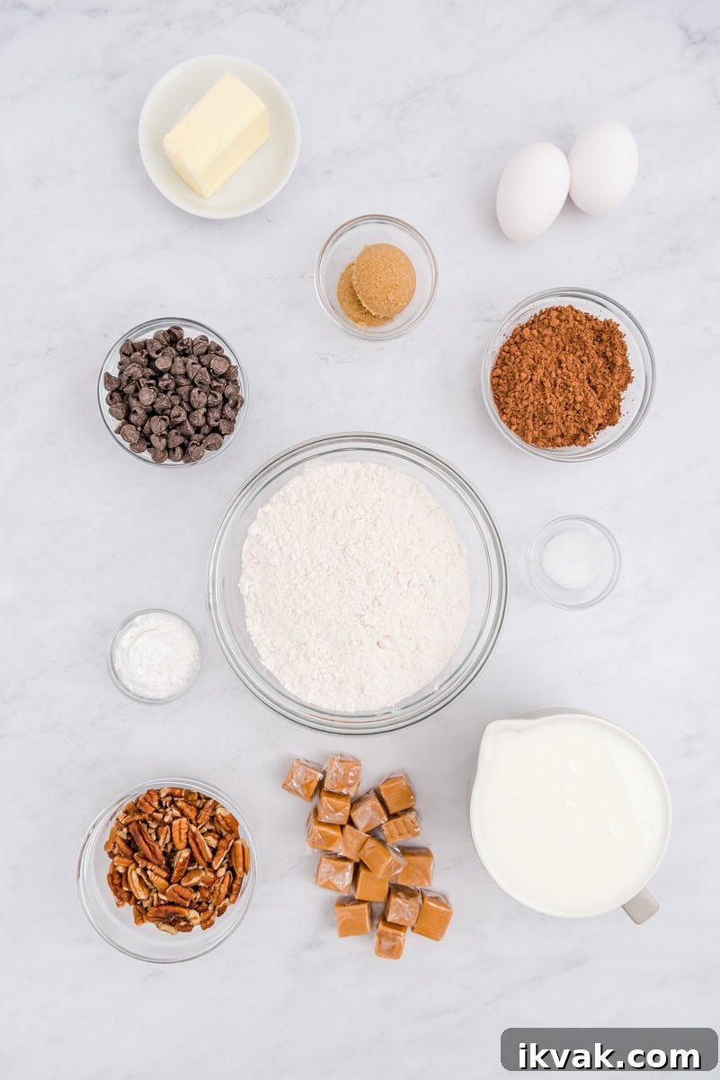 Ingredients on a marble surface including butter, eggs, brown sugar, cocoa powder, chocolate chips, baking powder, flour, pecans, caramels, salt, and buttermilk.