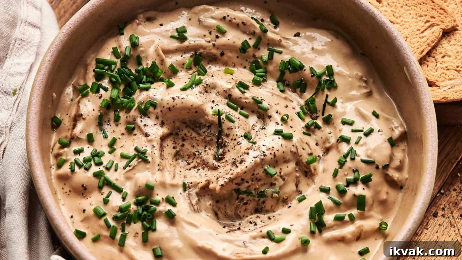 25 Creative Ways to Use Dip Recipes Beyond the Bowl 14 Bowl of creamy dip topped with chopped chives and black pepper, next to pieces of toasted bread.