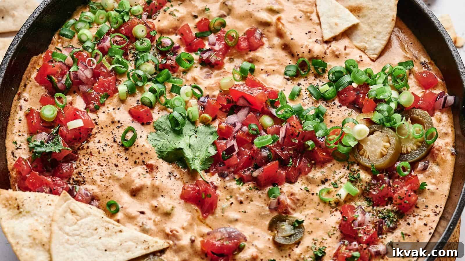25 Creative Ways to Use Dip Recipes Beyond the Bowl 19 A skillet filled with creamy cheese dip topped with chopped tomatoes, green onions, cilantro, and sliced jalapeños, surrounded by triangular tortilla chips.