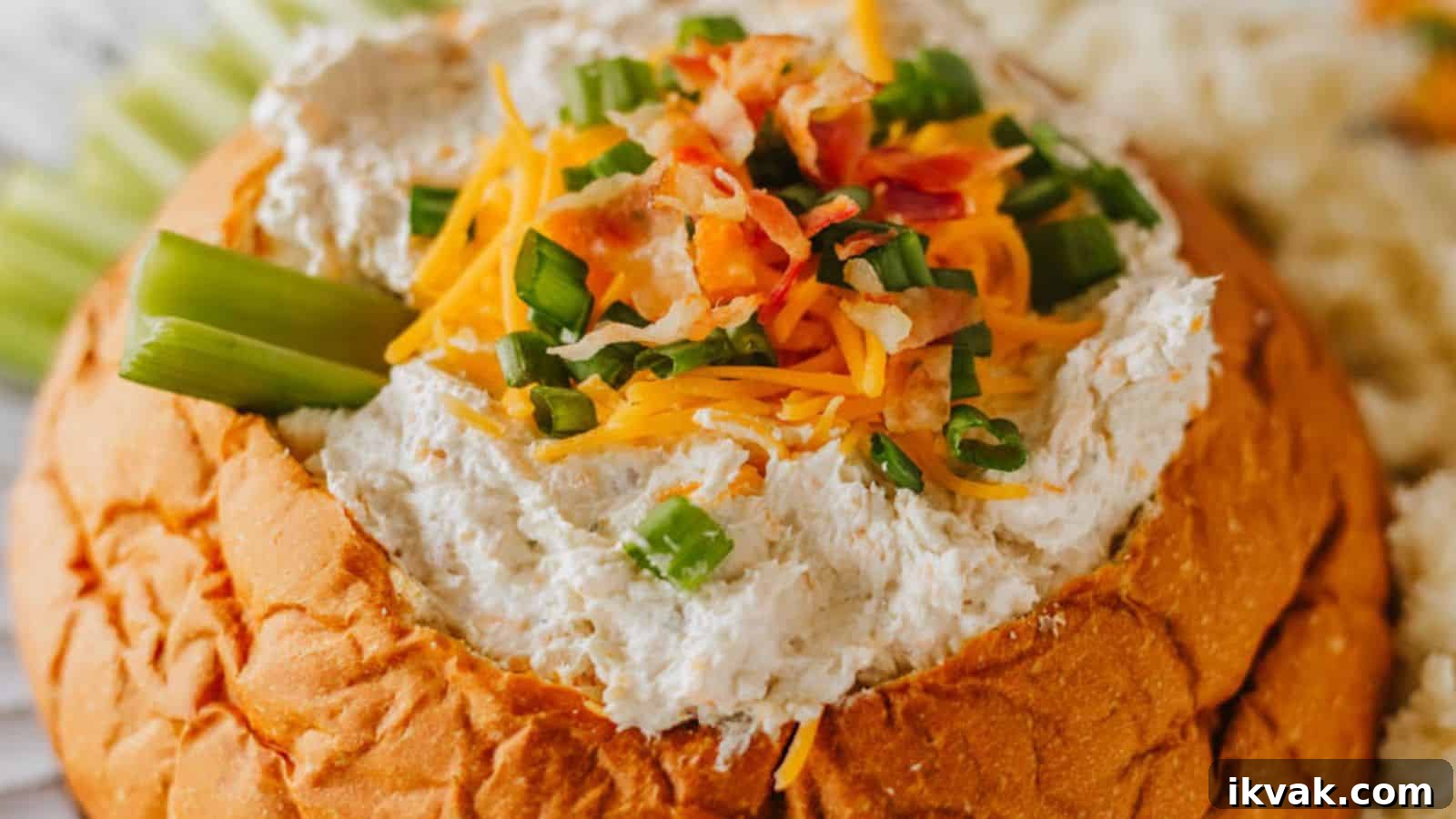 25 Creative Ways to Use Dip Recipes Beyond the Bowl 23 A bread bowl filled with a creamy dip, garnished with shredded cheese, chopped green onions, and bacon bits. Celery sticks are placed on the side.