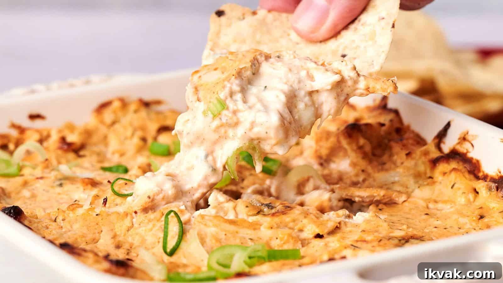 25 Creative Ways to Use Dip Recipes Beyond the Bowl 5 A hand dips a tortilla chip into a cheesy baked dish topped with sliced green onions.