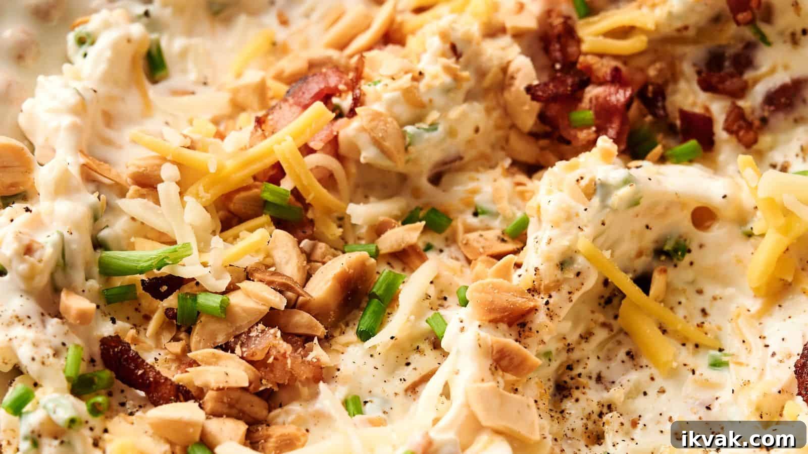 25 Creative Ways to Use Dip Recipes Beyond the Bowl 6 Close-up of a creamy dish topped with shredded cheese, chopped nuts, bacon bits, and sliced green onions.