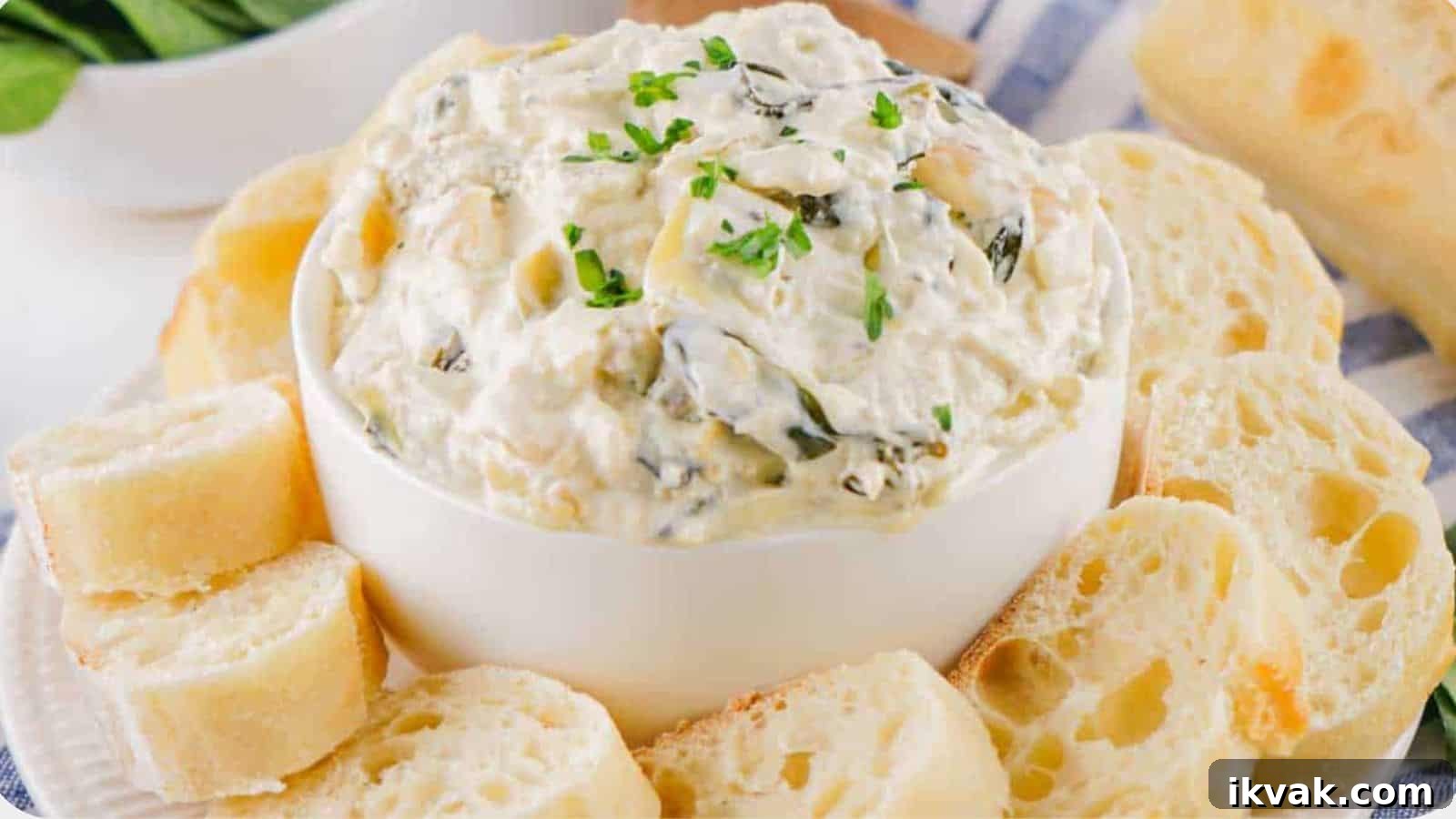 25 Creative Ways to Use Dip Recipes Beyond the Bowl 7 A bowl of creamy spinach dip garnished with herbs, surrounded by slices of crusty bread on a blue patterned cloth.