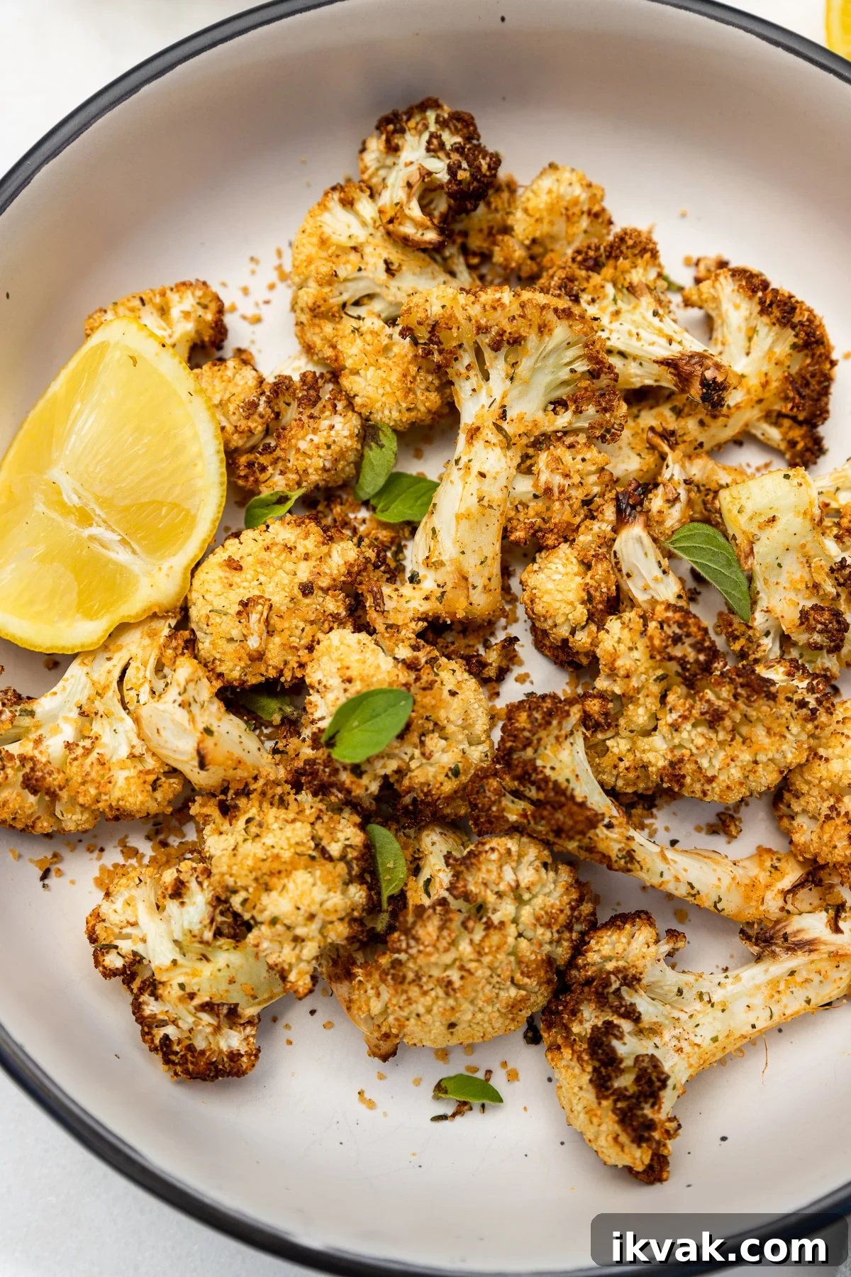 Closeup of an overhead view of a big bowl of air fried cauliflower with lemon and fresh herbs on top.