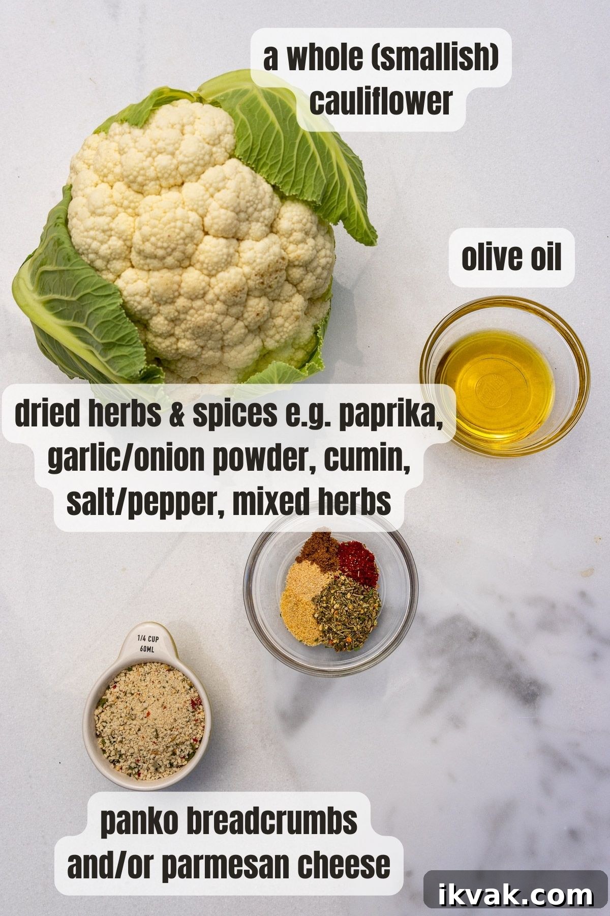 All the ingredients needed for air fryer cauliflower including a head of cauliflower, a mix of herbs and spices, olive oil and panko crumbs and parmesan, all on a marble background.