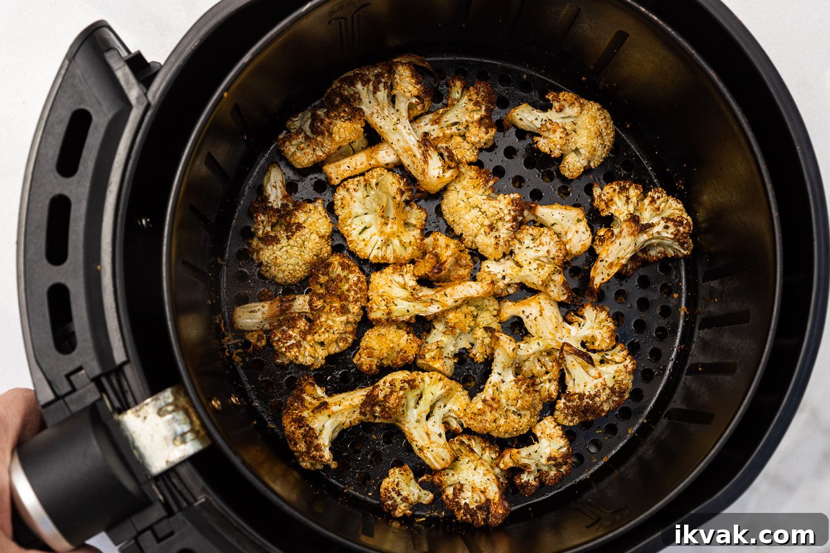 Someone holding an air fryer basket with golden air fried cauliflower in it.