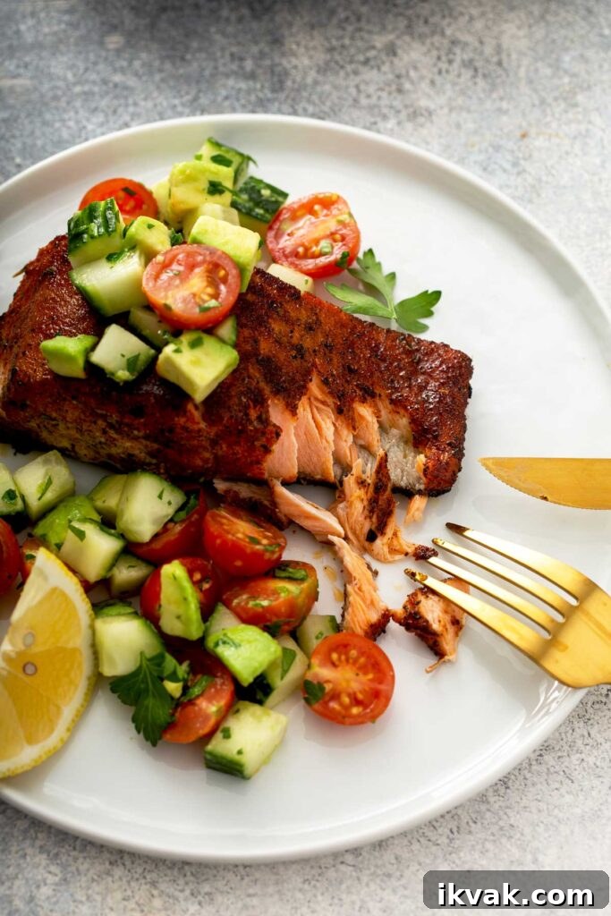 Blackened Salmon Recipe: Quick Cajun-Style Pan-Seared Fillets 4 Flaky salmon fillet with blackening spices on a white plate topped with cucumber, tomatoes and avocado salad