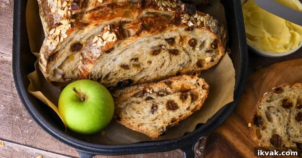 Apple Crisp Sourdough Loaf 3 Sourdough apple crisp loaf sliced open so you can see the inside. The loaf is displayed inside a cast iron bread pan with a green apple next to it.