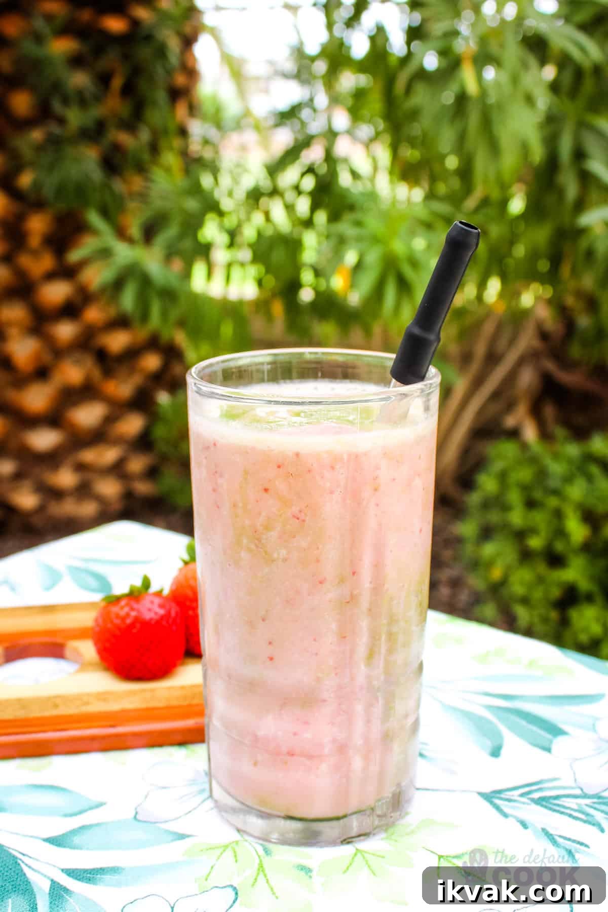 Creamy Strawberry Matcha Smoothie Recipe 2 Smoothie on a table outdoors with strawberries and greenery behind it.
