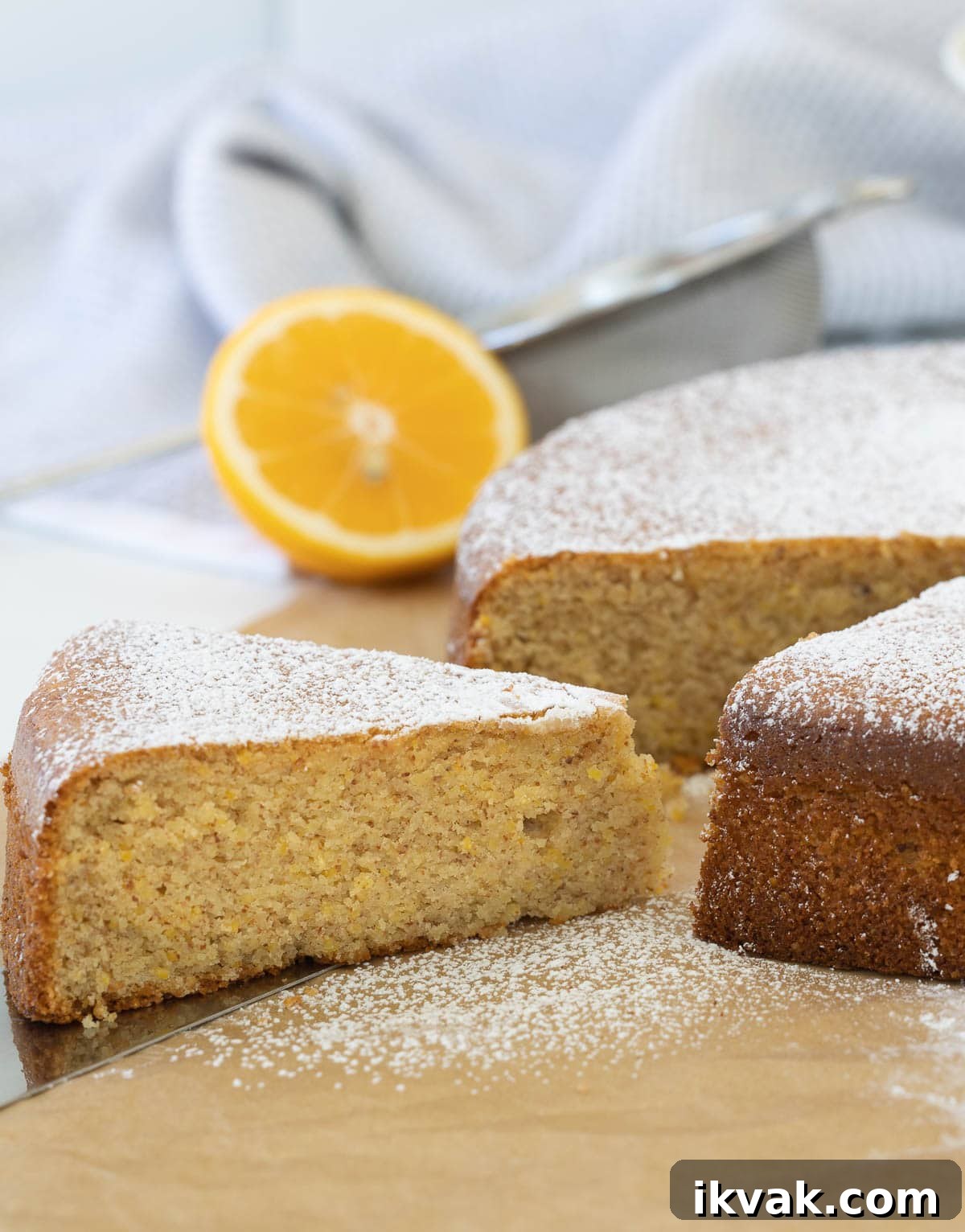 The olive oil cake on the counter, a piece cut out dusted with powdered sugar.