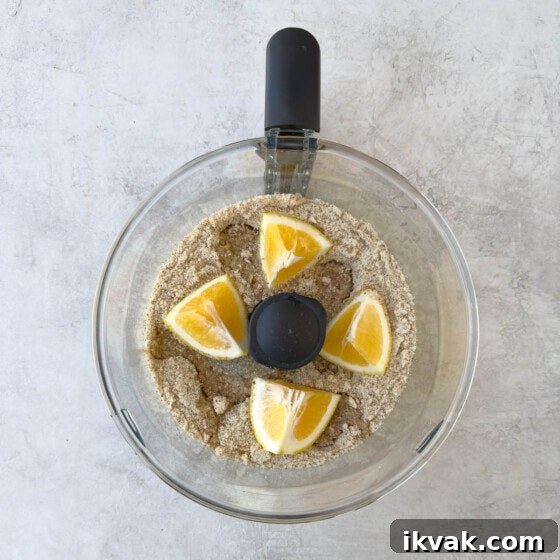 Grinding whole almonds, sugar, and lemon in a food processor bowl.