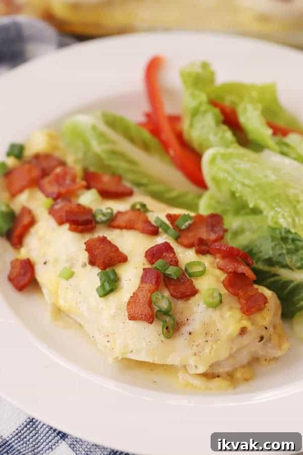 a plate with baked honey mustard chicken topped with bacon bits, sliced green onions, and a side salad. 