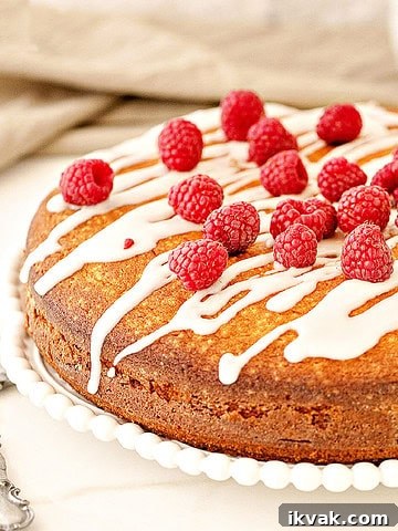Raspberry coffee cake with glaze and fresh berries on a white plate. White surface, beige background.