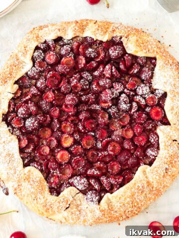 Whole baked cherry galette on a white surface.