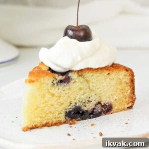 Moist Cherry Cake with Fresh Cherry Glaze 14 Cream topped cherry cake slice on a white plate. Close up image.