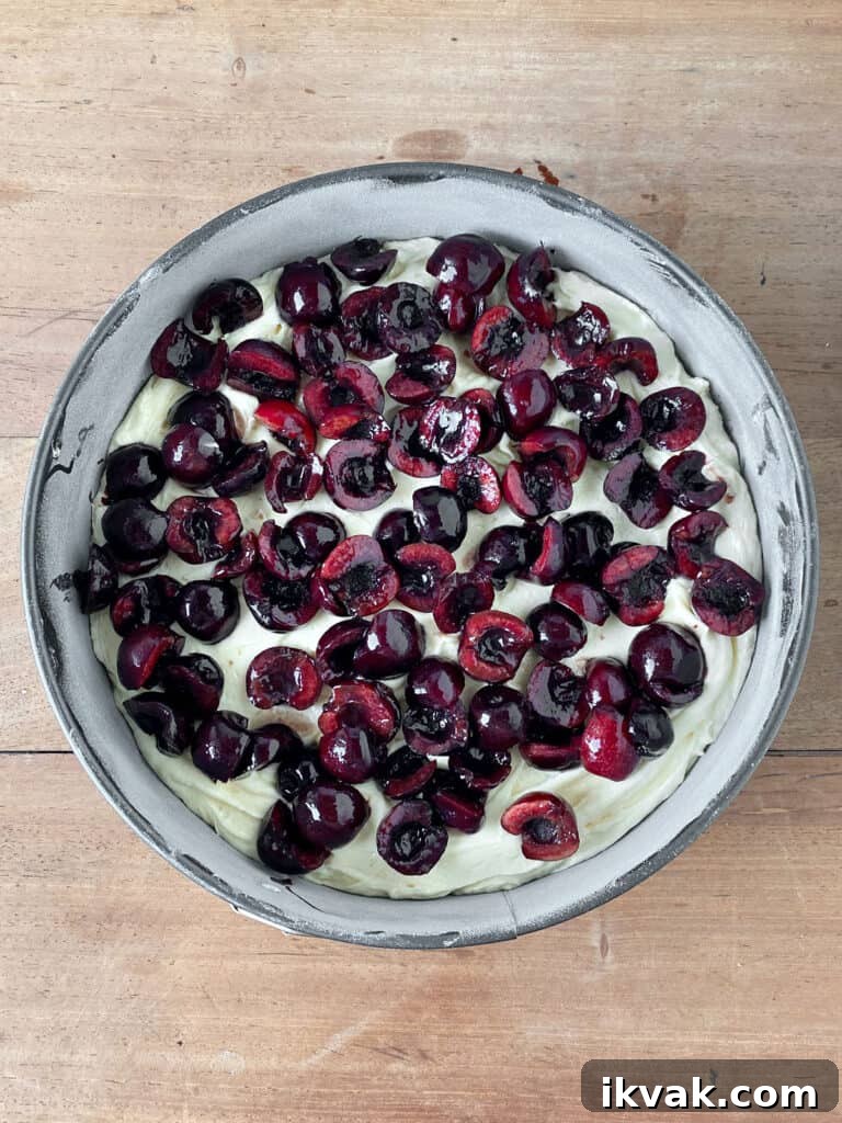 Moist Cherry Cake with Fresh Cherry Glaze 7 Fresh halved cherries topping cake batter in a round pan. Wooden surface.