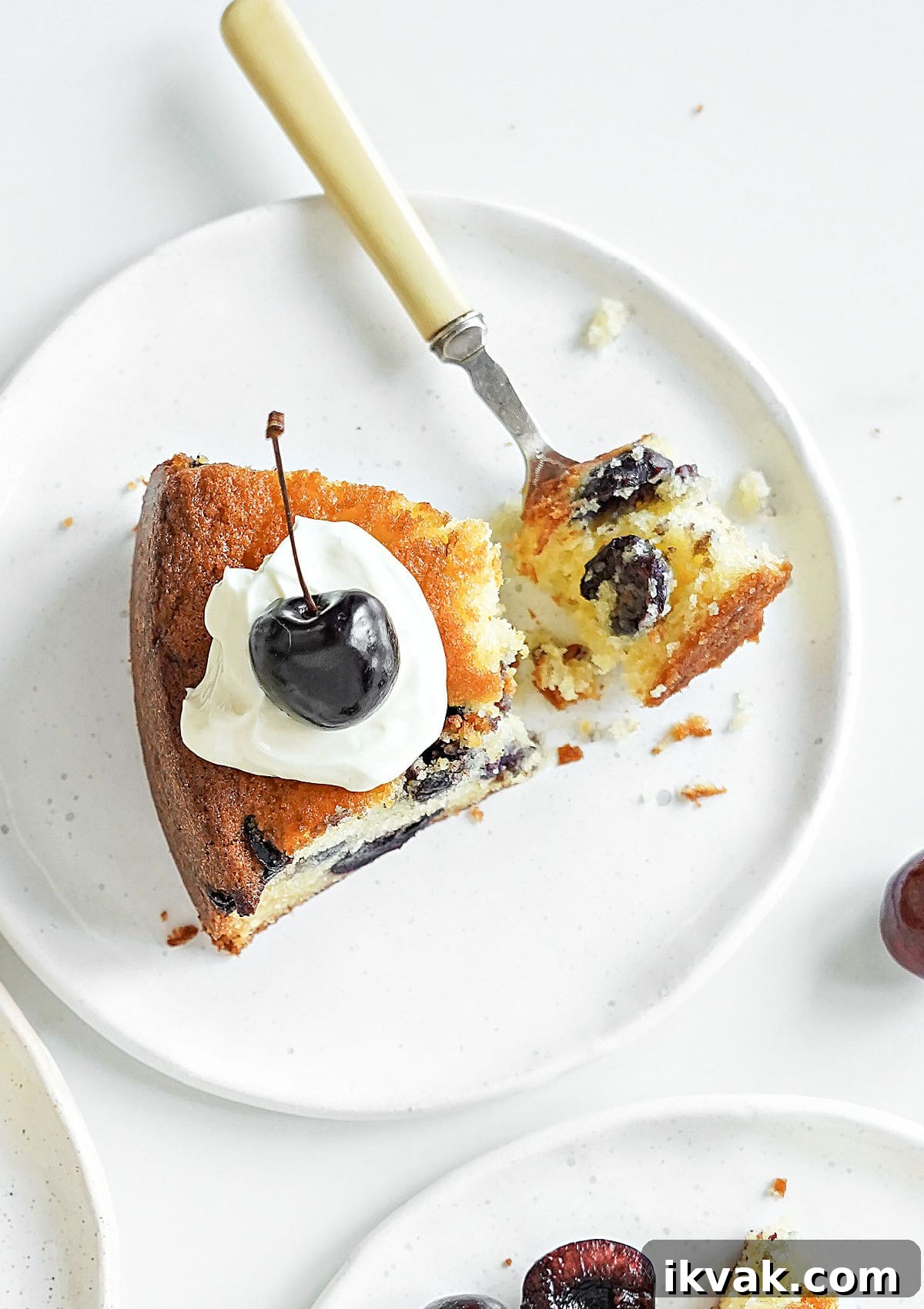 Moist Cherry Cake with Fresh Cherry Glaze 9 Slice of cherry cake with cream on a white plate. Fork with a bite. White background.