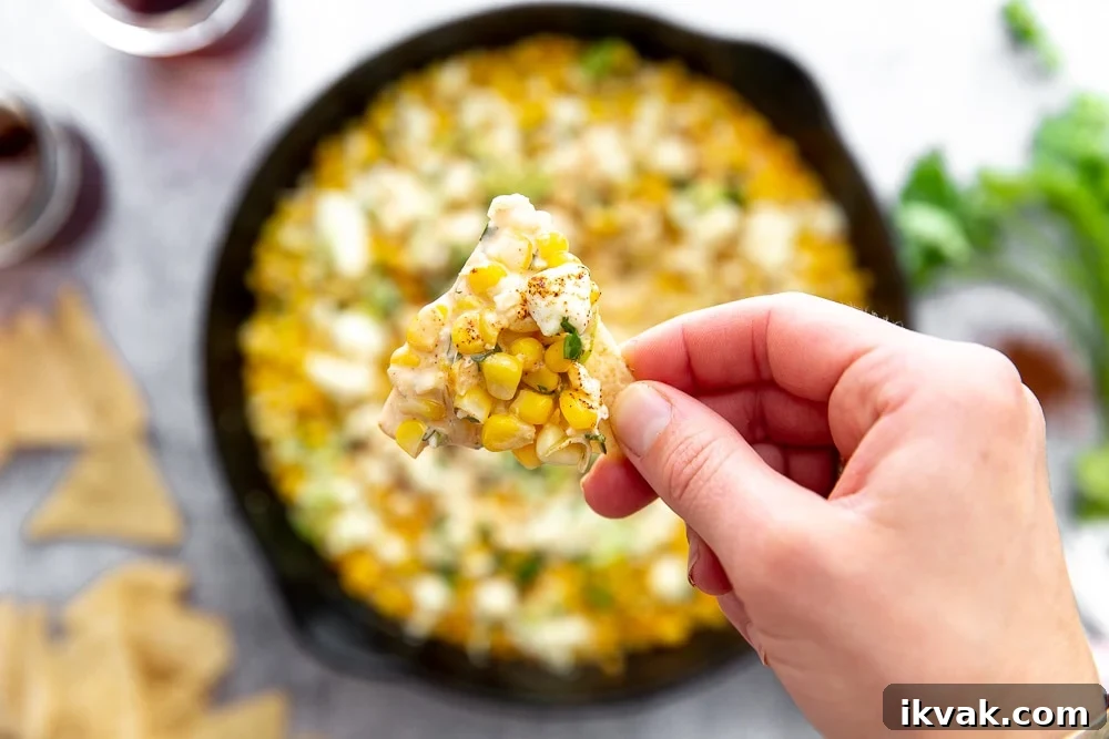 Close up overhead shot of hand holding tortilla chip topped with Mexican street corn dip.
